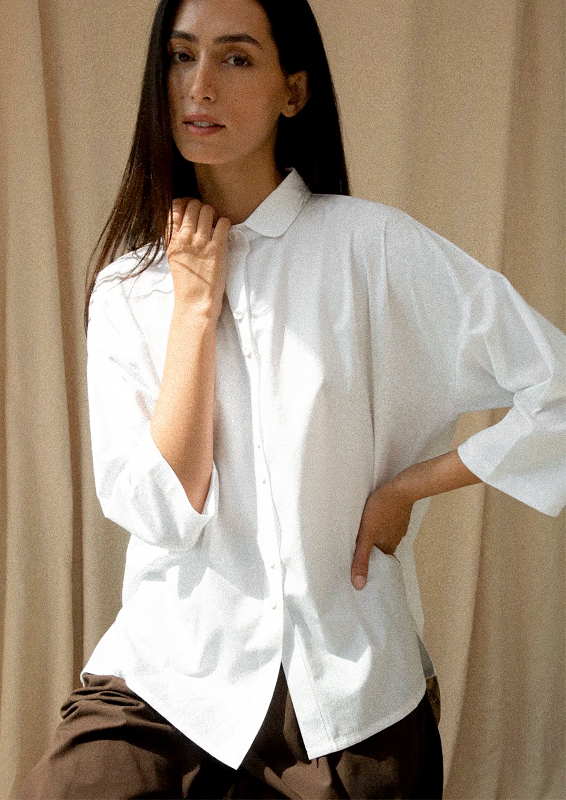 Woman wearing a white shirt against a beige curtain background