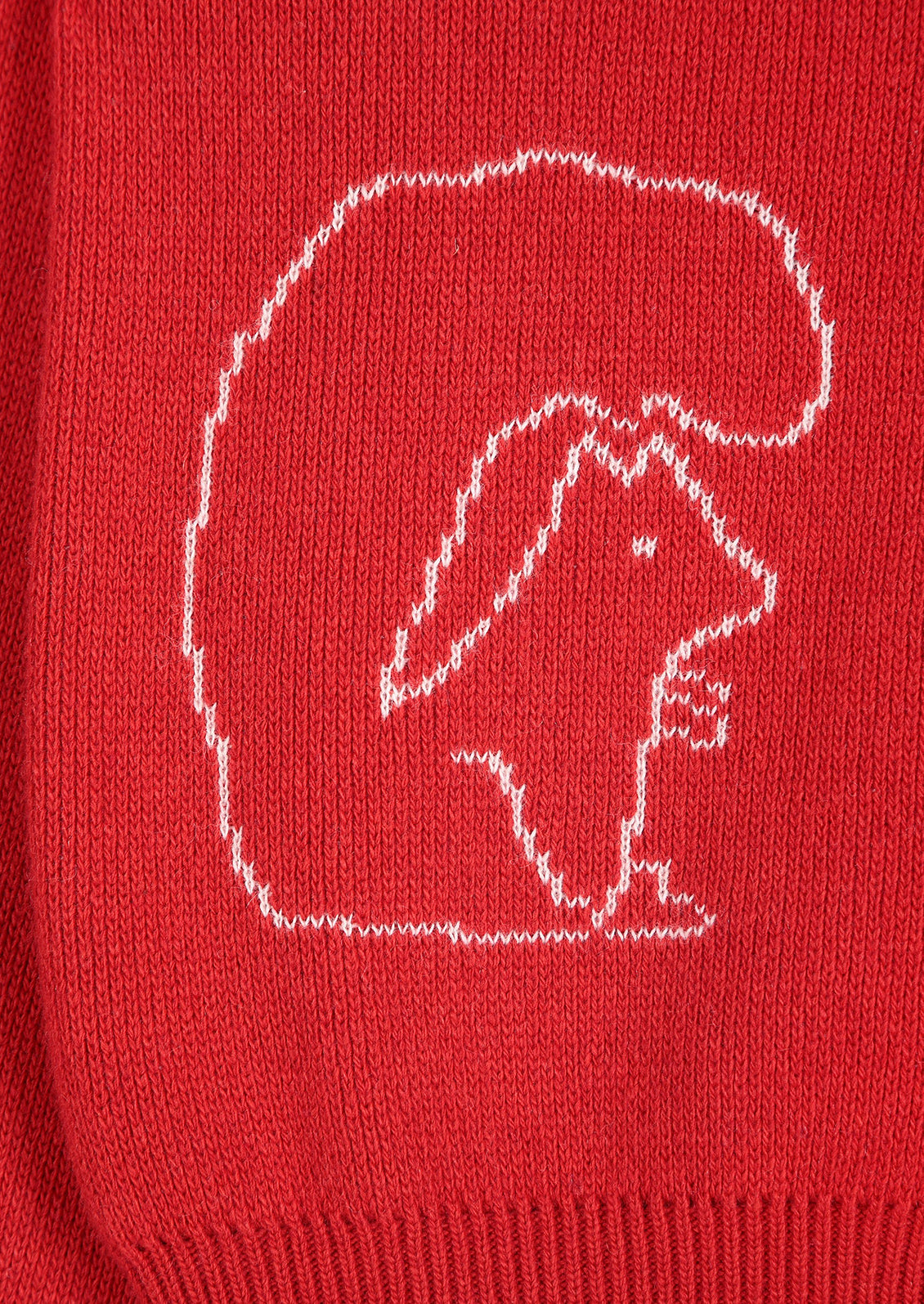 Close-up of a red knit garment featuring a white knitted outline of a squirrel inside a large rounded shape.