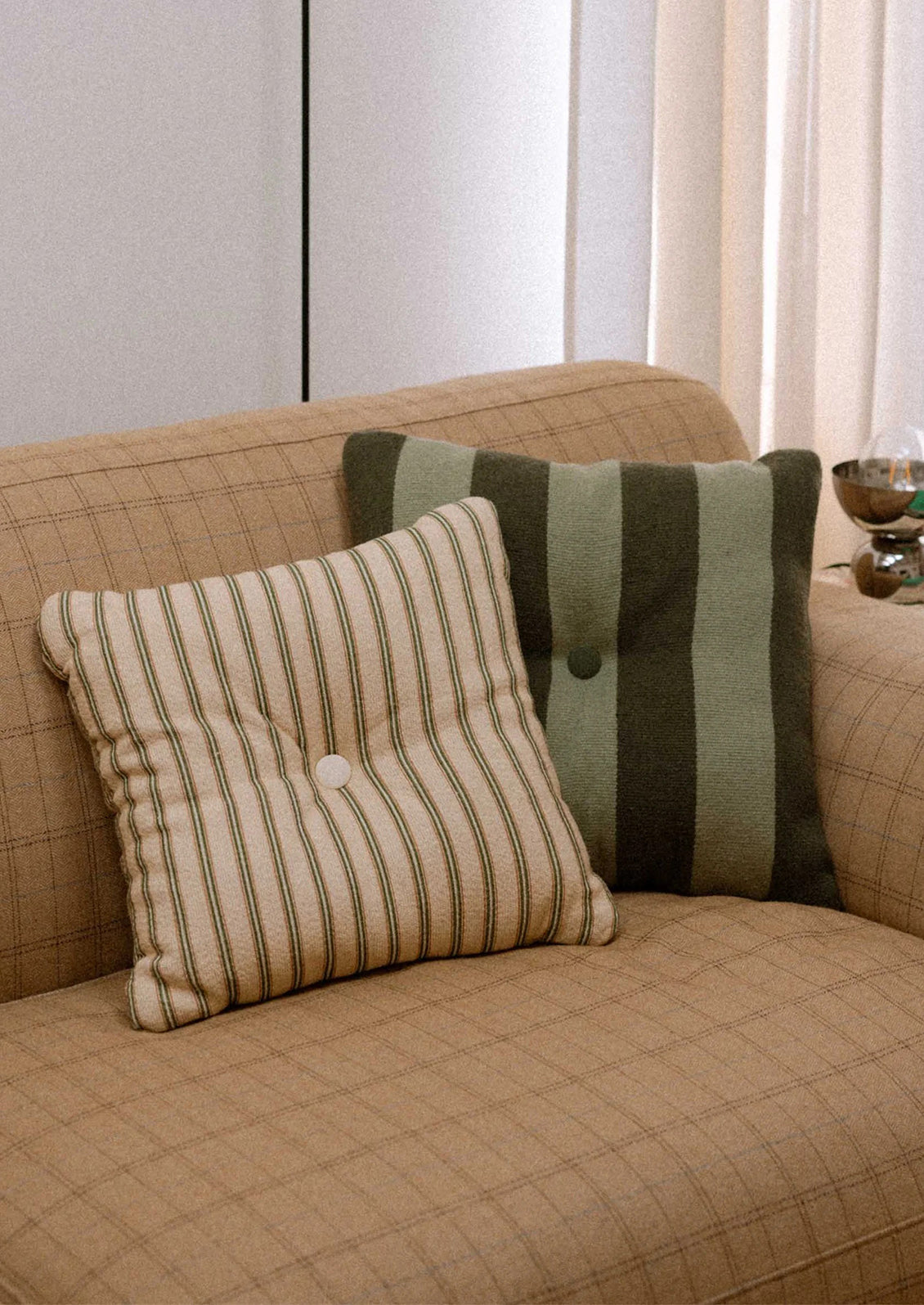 A striped pillow in mint and grey green with tufted button detail at center.