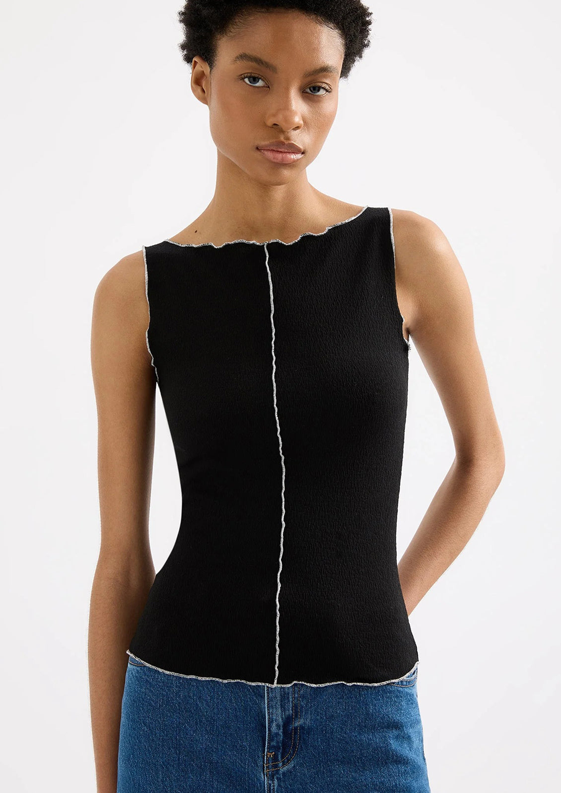 Woman wearing a black sleeveless top with white trim on a white background