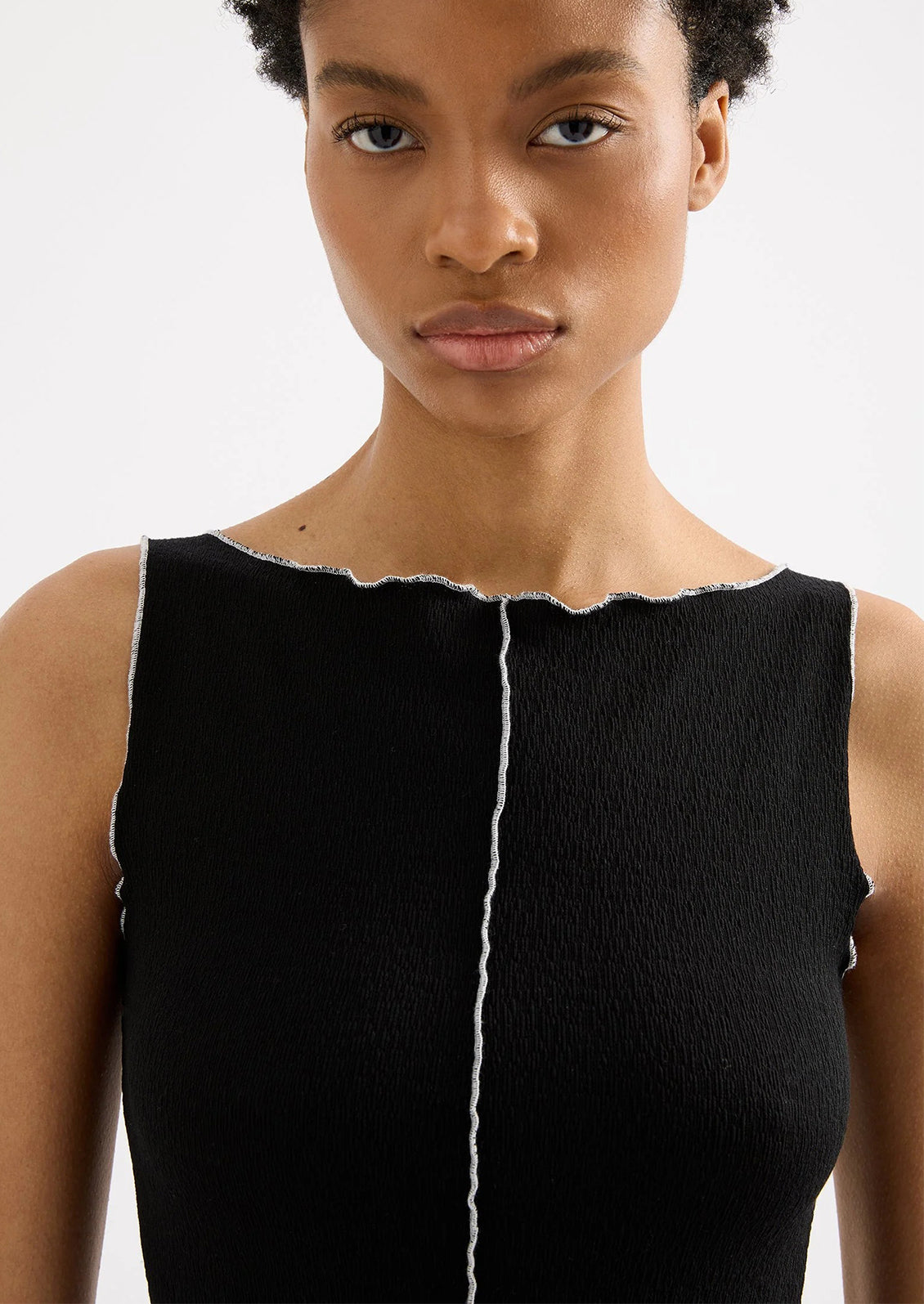Woman wearing a black sleeveless top with a white stripe on a plain background