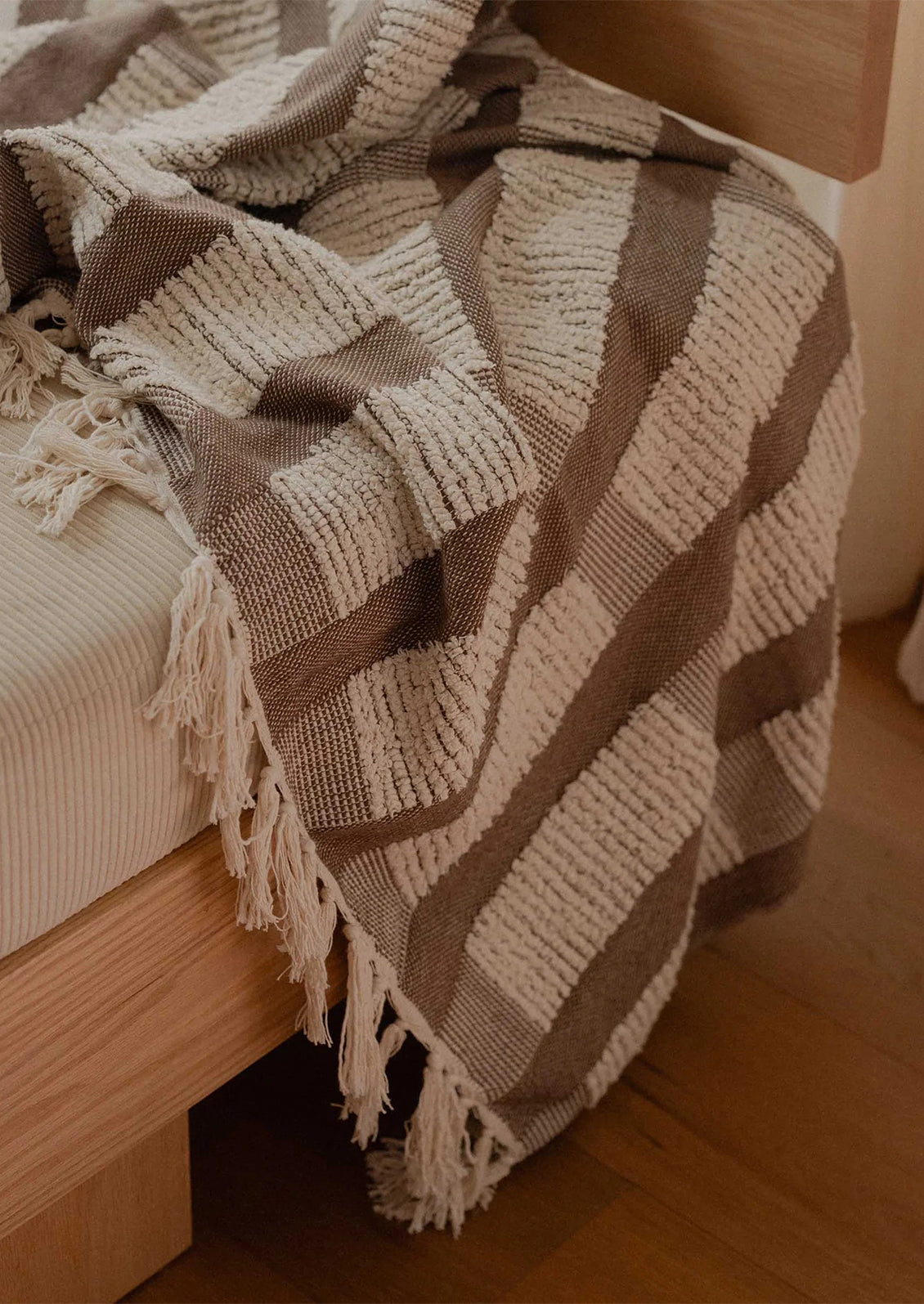 Textured blanket with fringes draped over a wooden bed frame.