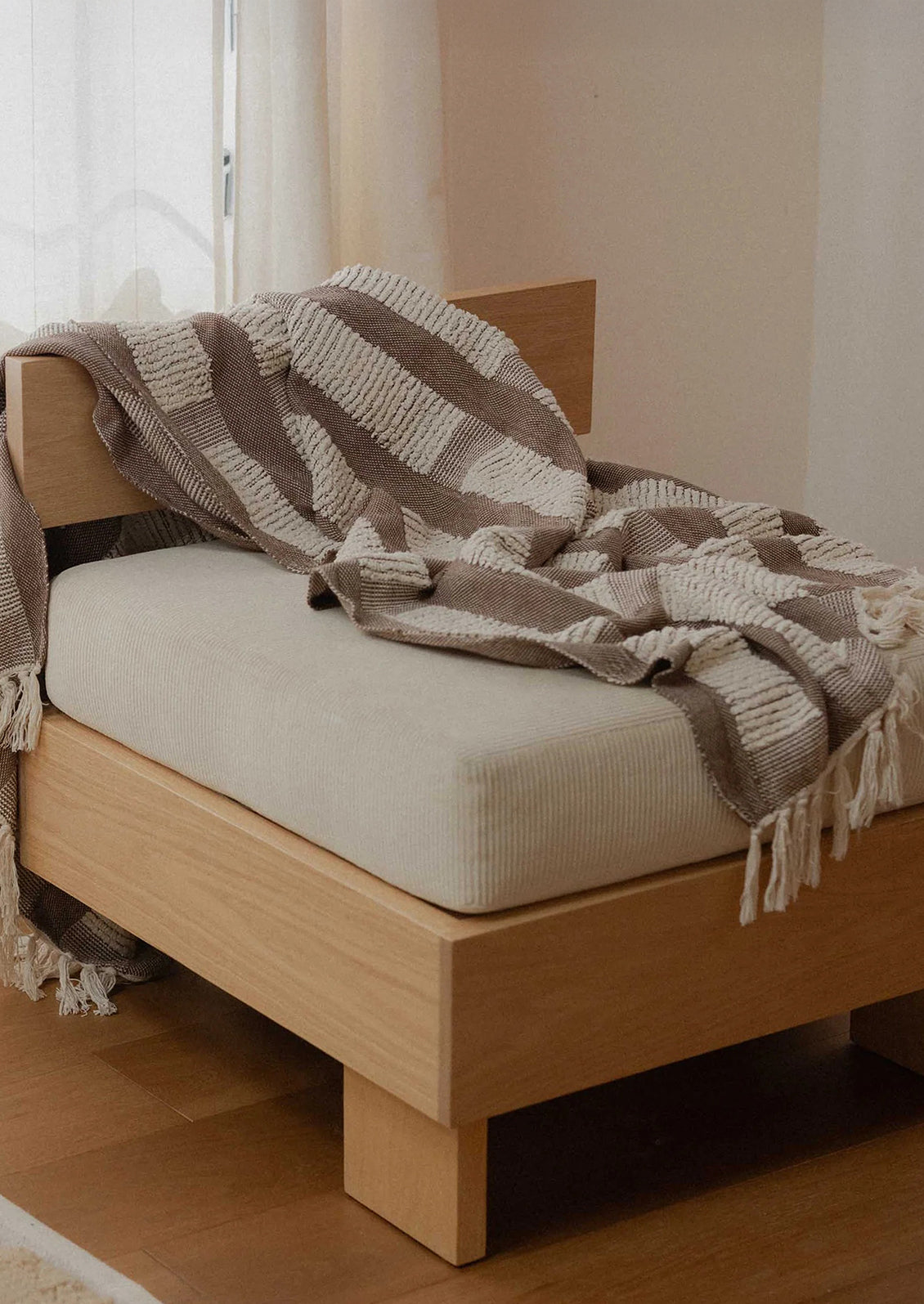 Wooden bed with beige mattress and striped blanket in a room.