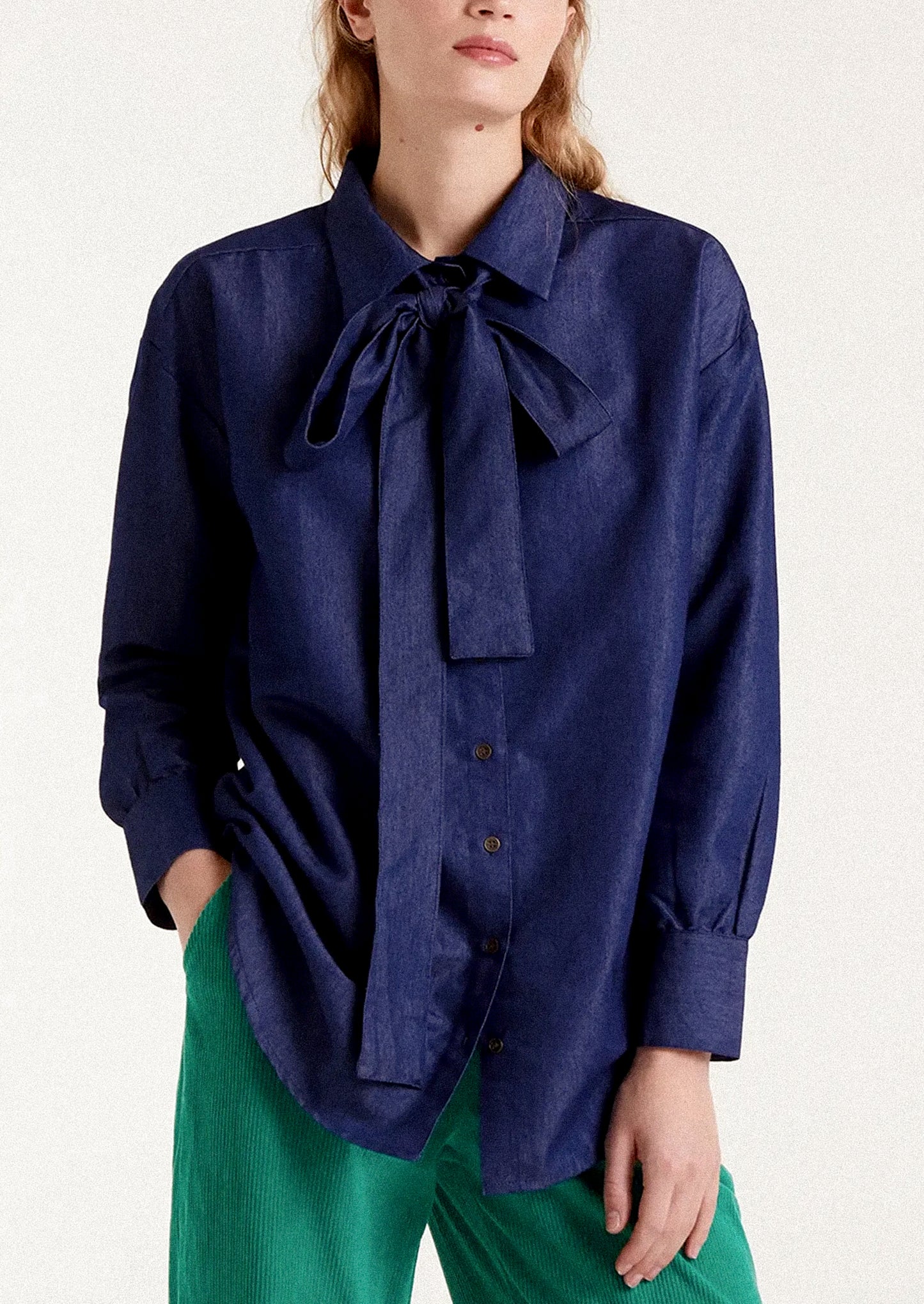 A woman wearing a dark blue chambray shirt with tie detail at neckline.