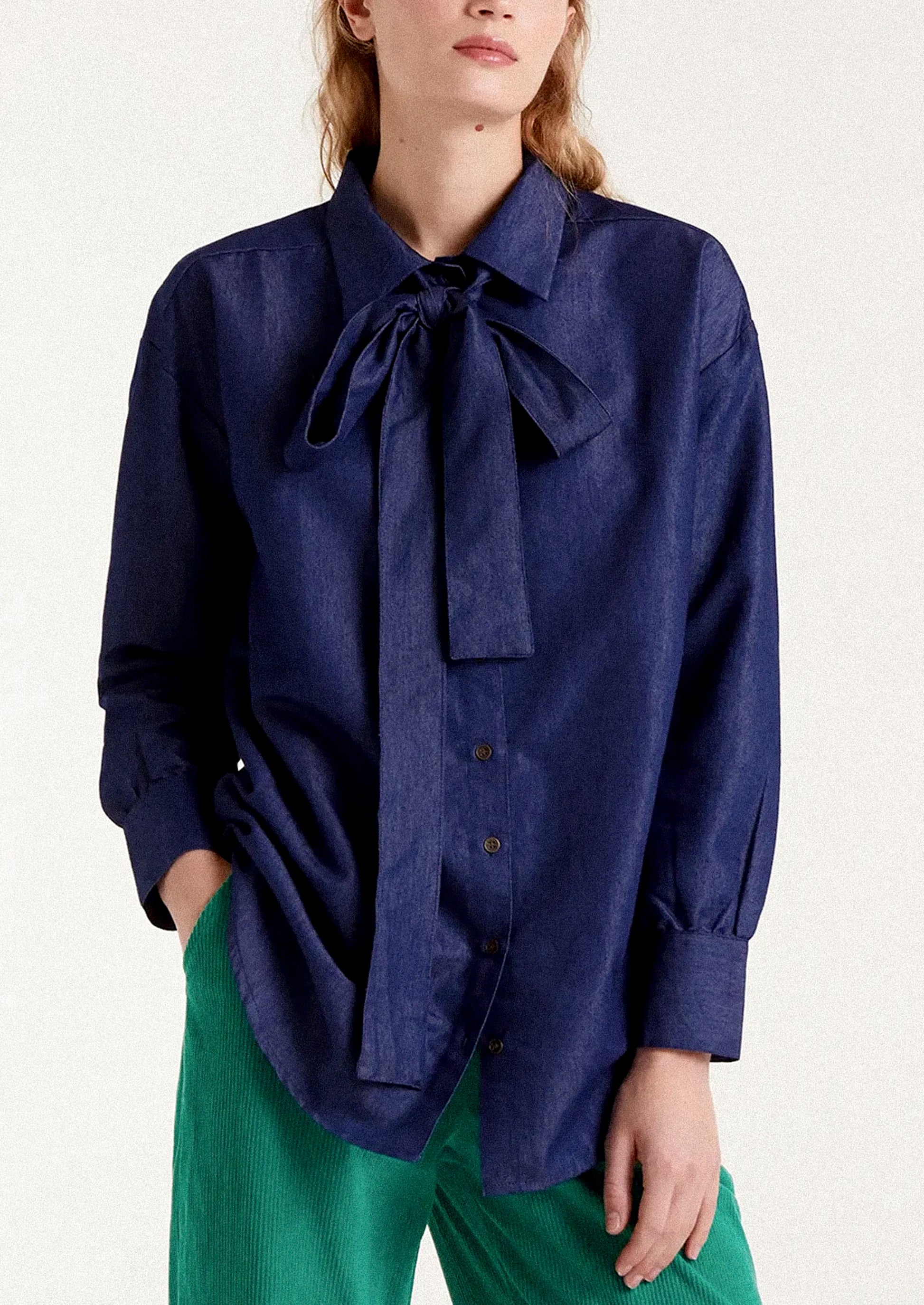 A woman wearing a dark blue chambray shirt with tie detail at neckline.