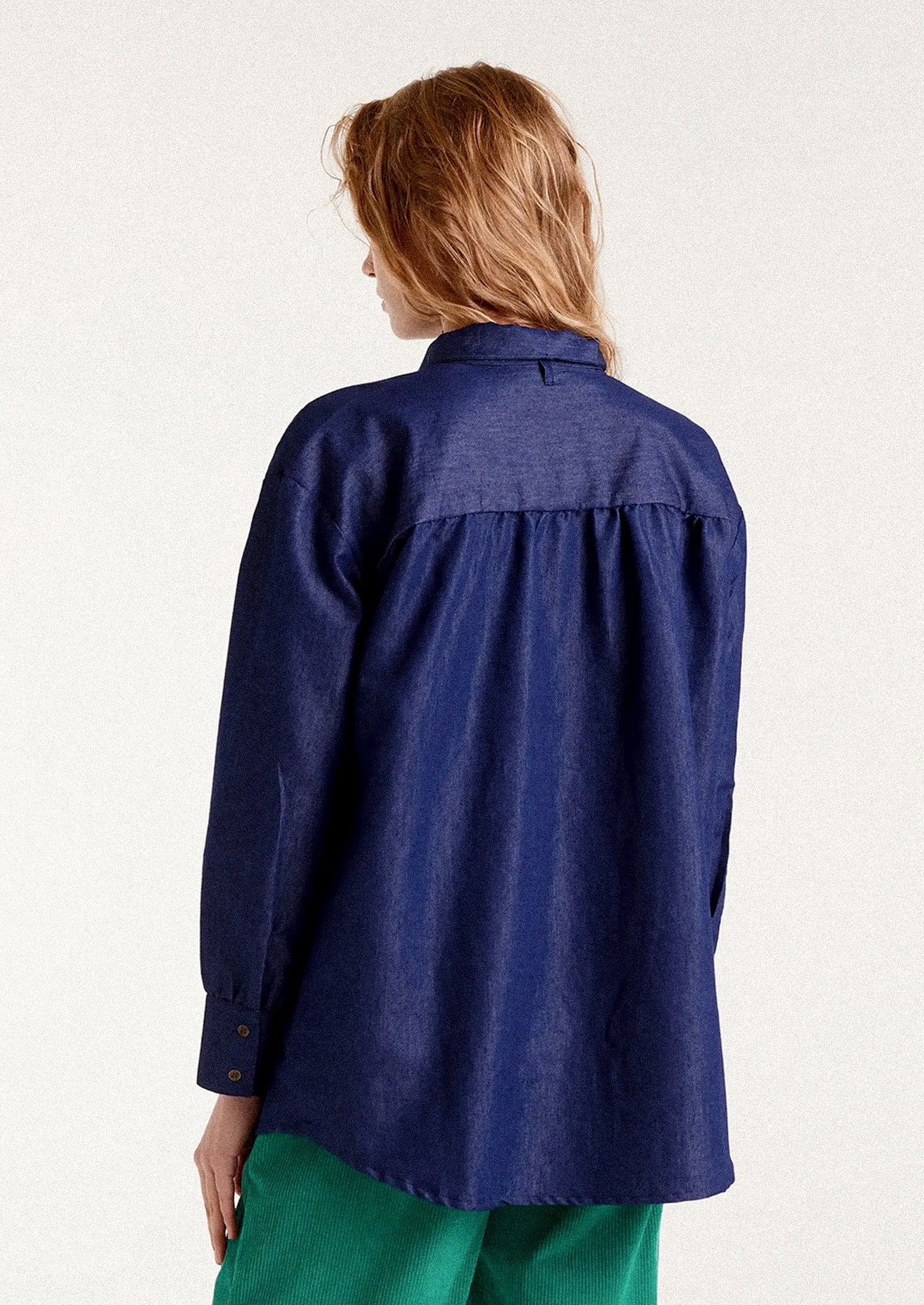 A woman wearing a dark blue chambray shirt with tie detail at neckline.