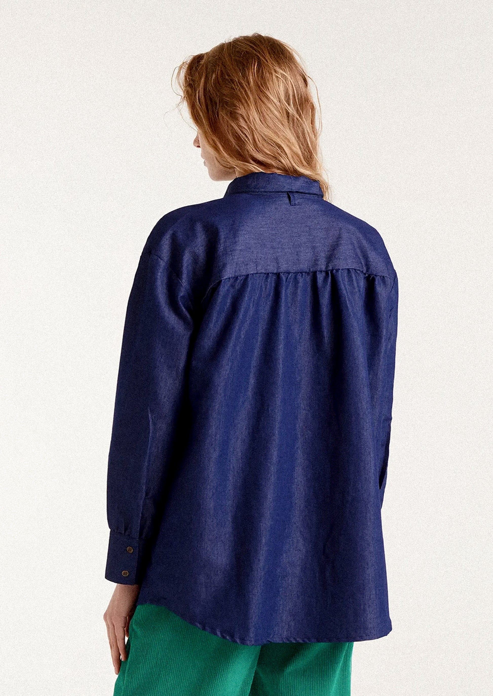 A woman wearing a dark blue chambray shirt with tie detail at neckline.