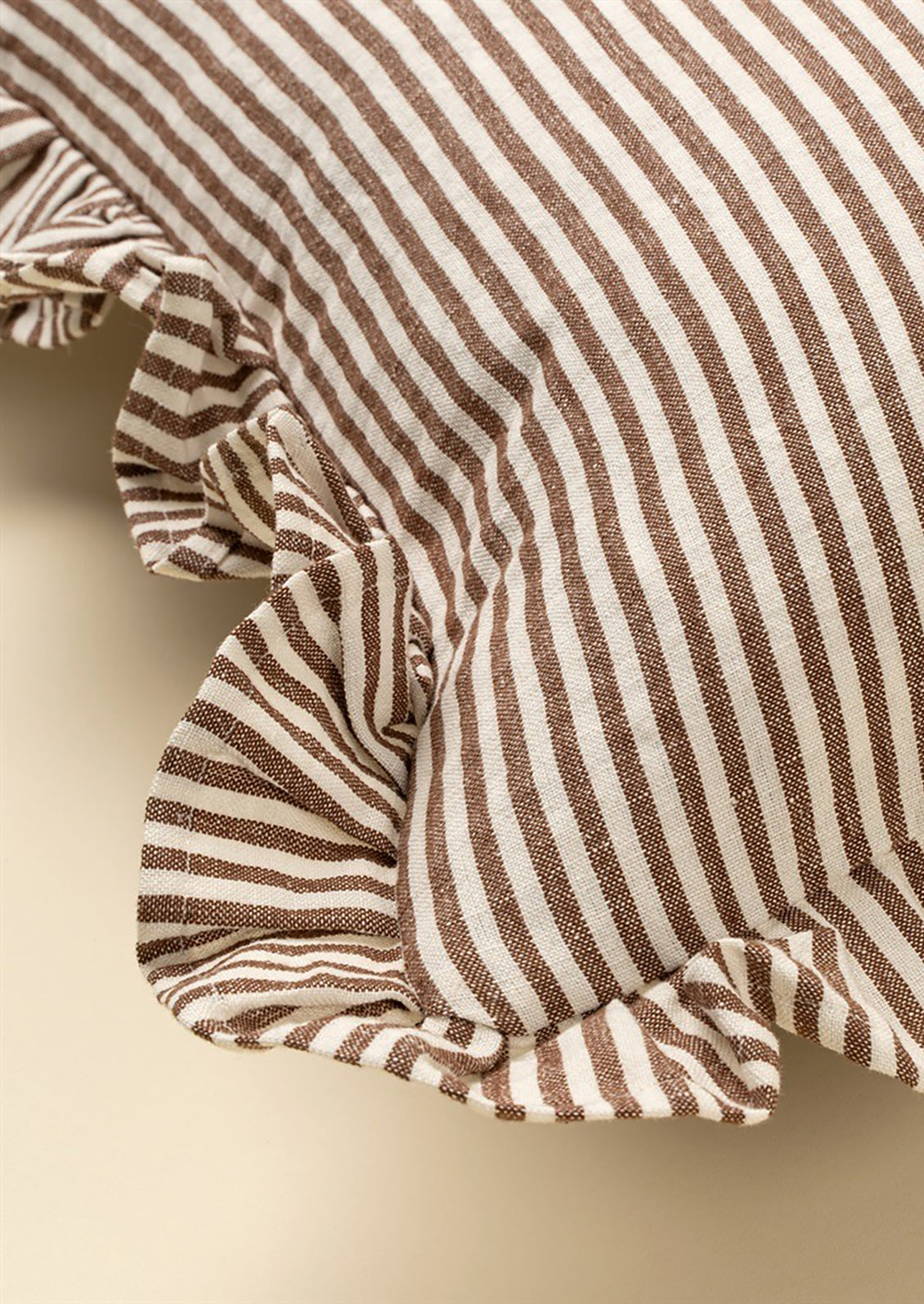 Close-up of a brown and white striped fabric with ruffled edges on a beige background