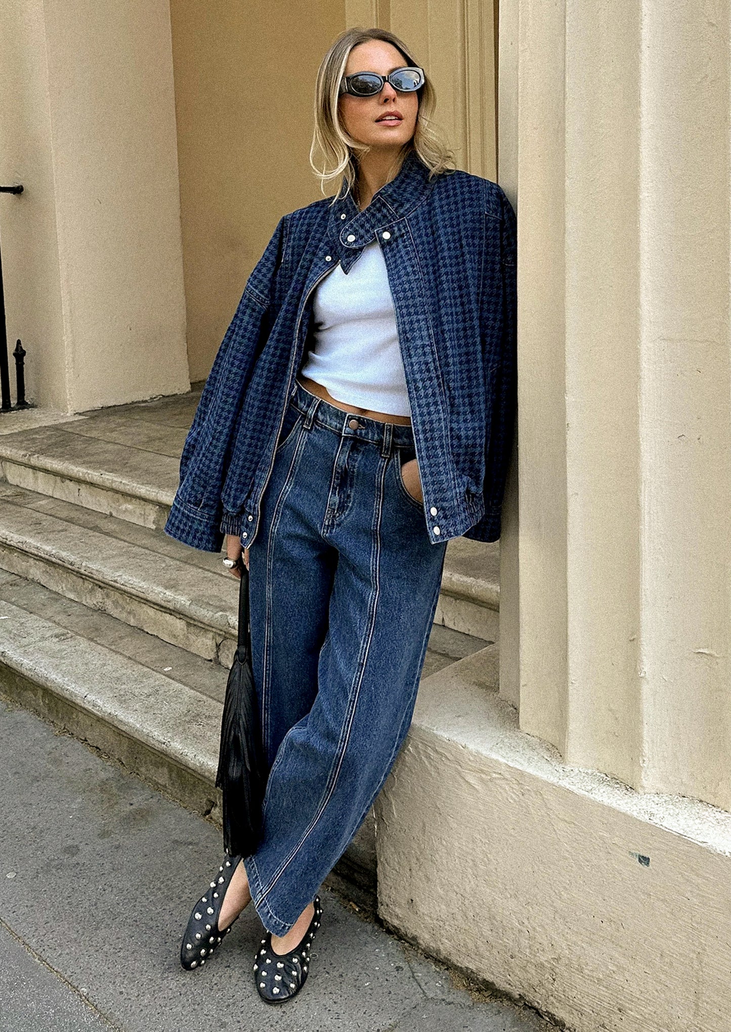 Woman in blue plaid shirt, white top, and jeans standing on steps with a building in the background