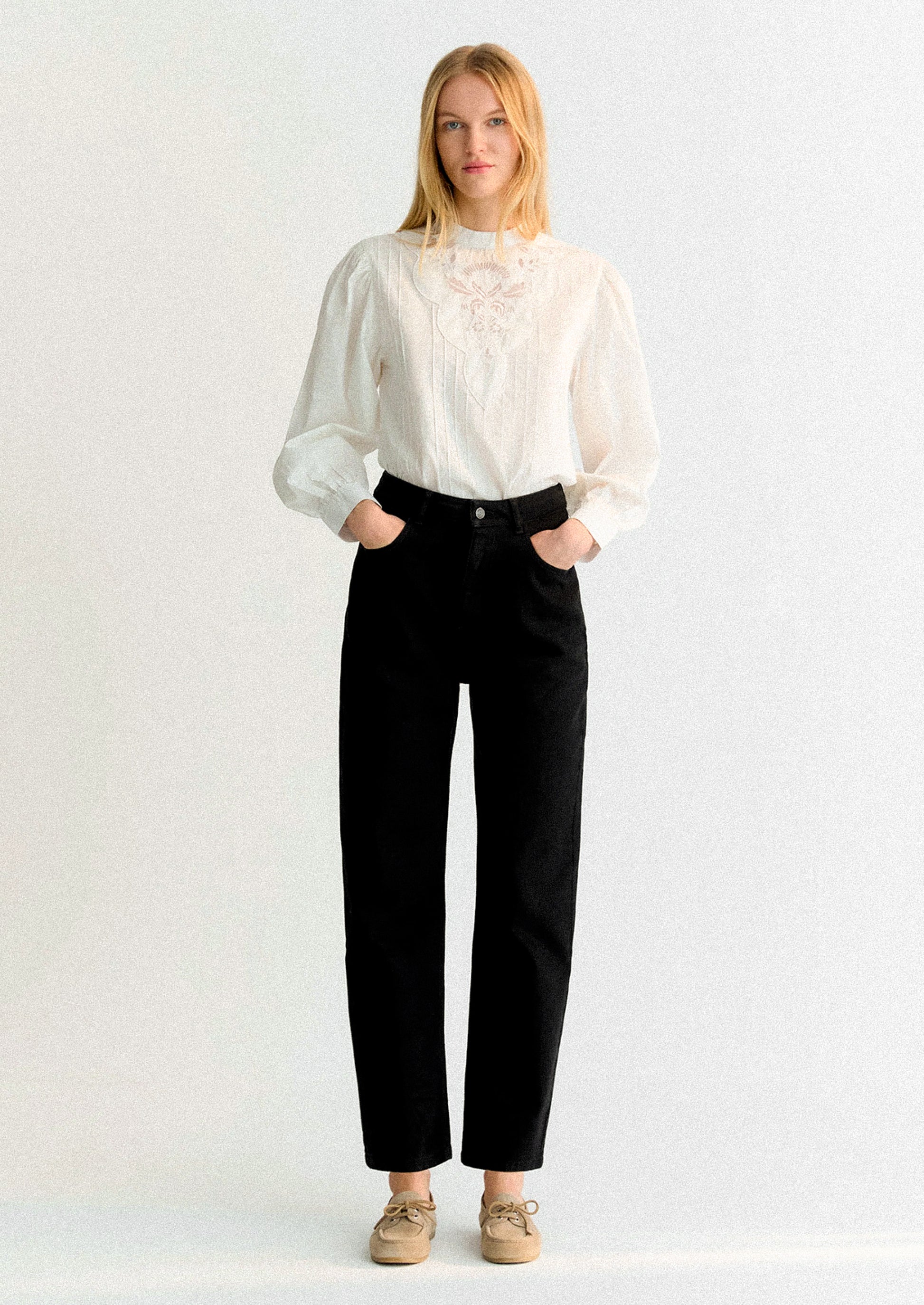 Woman wearing a white blouse and black pants on a white background.