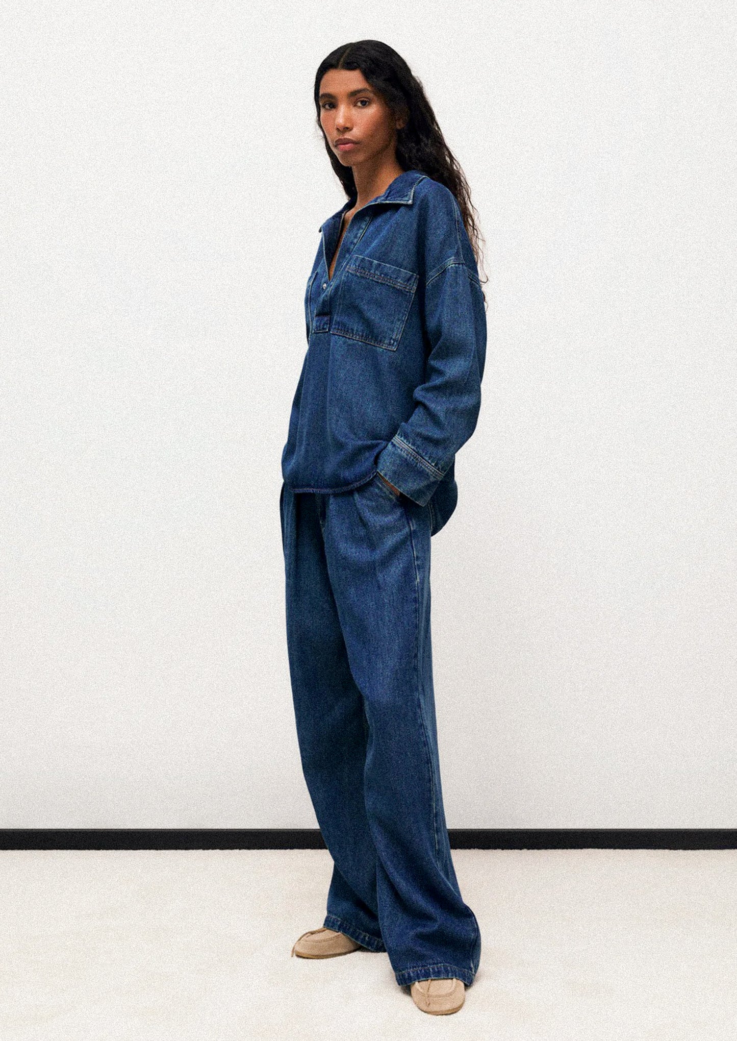 A woman wearing a pair of pleat front wide leg pants in blue denim.