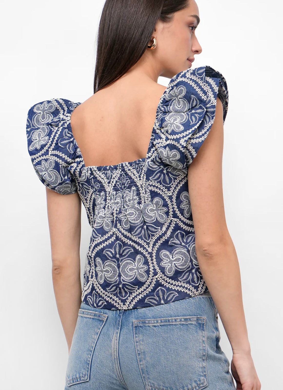 Woman wearing a blue and white embroidered top with ruffled shoulders.