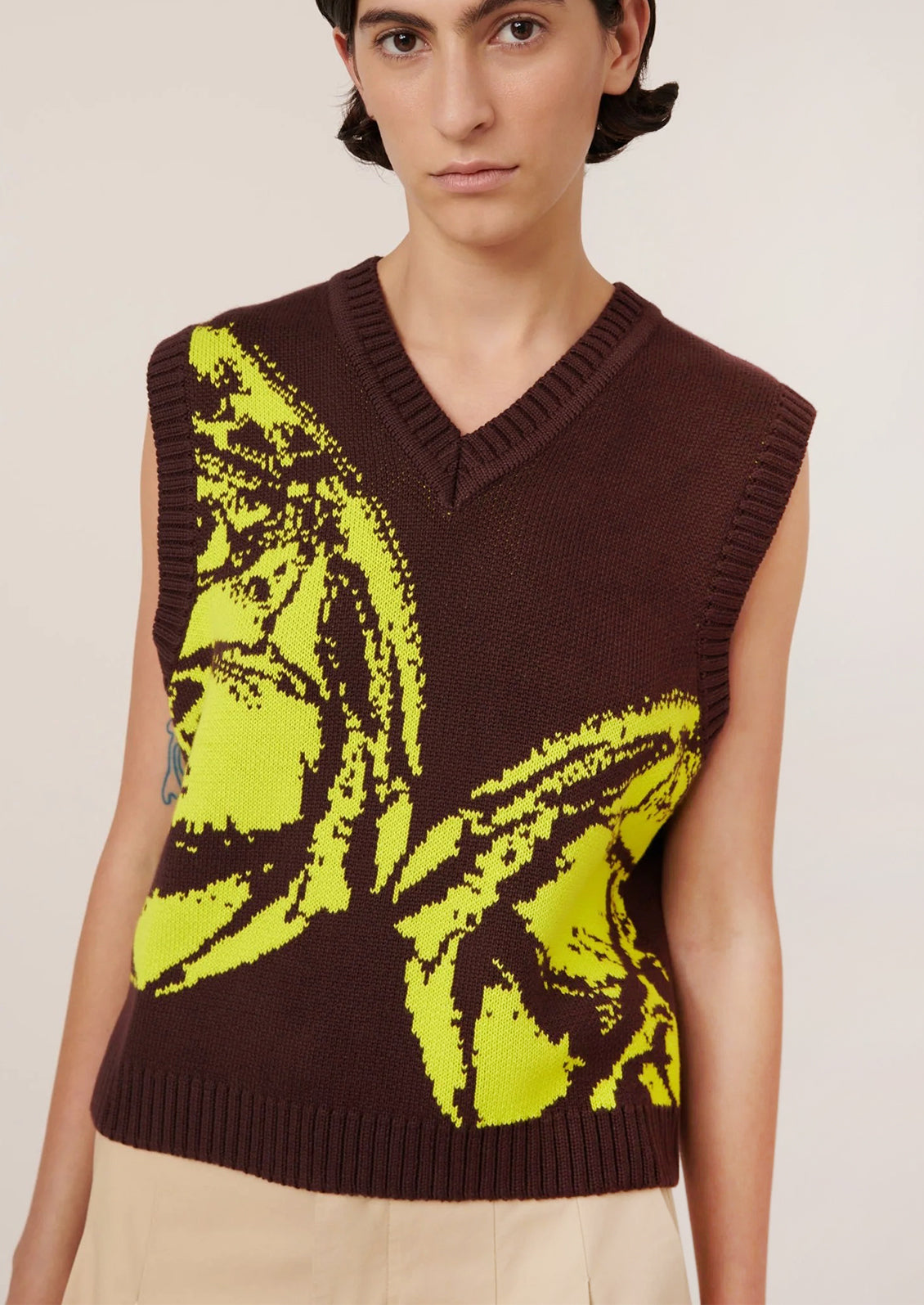 Person wearing a brown knit vest with a large yellow butterfly design.