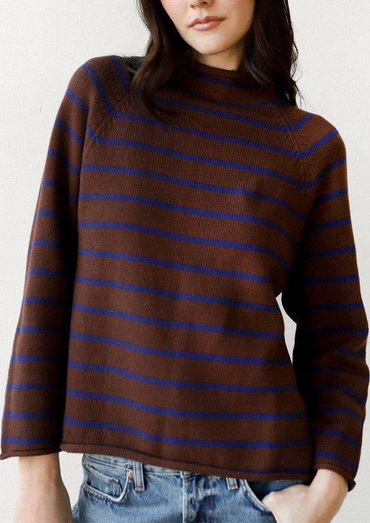 A woman wearing a brown knit mock-neck sweater with thin horizontal blue stripes, paired with blue jeans, shown against a plain off-white background.