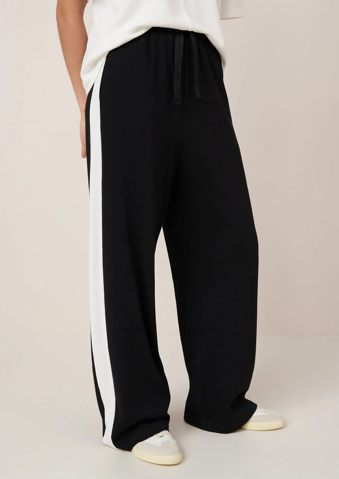 Black pants with white stripes worn by a person on a beige background