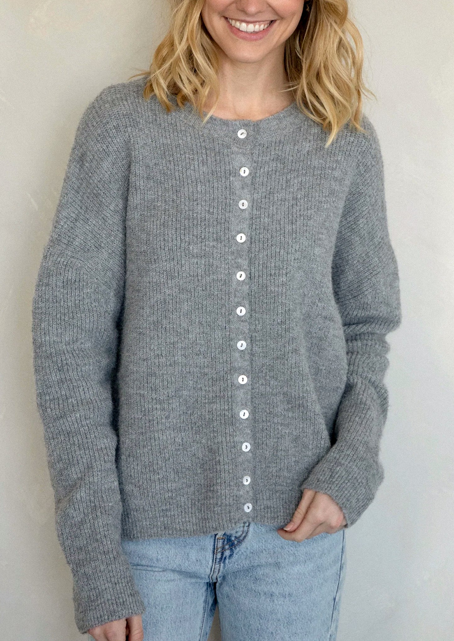 A woman wearing a heather grey cardigan with white button front.