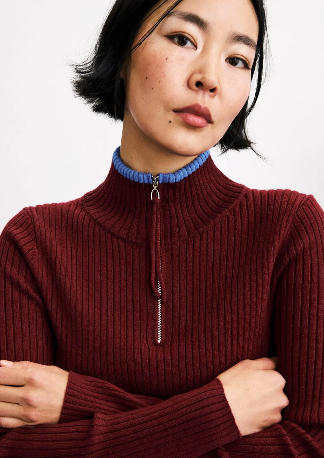 A person wearing a wine red ribbed sweater with mock neck with small blue trim at edge.