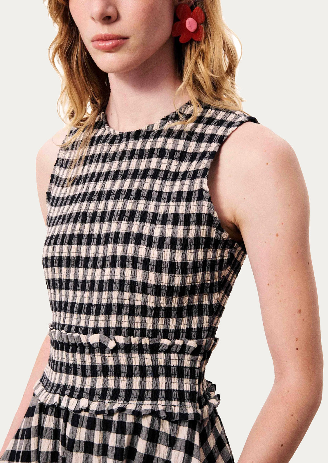 A close-up of a woman wearing a sleeveless black and beige gingham dress with a smocked waist and ruffled details.
