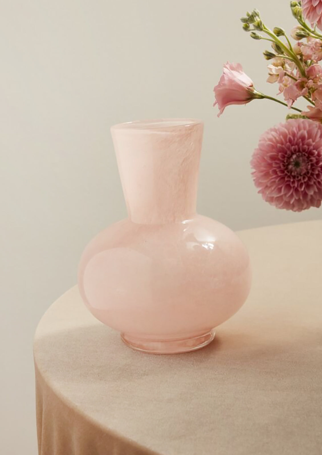 Pink vase on a table with pink flowers in the background