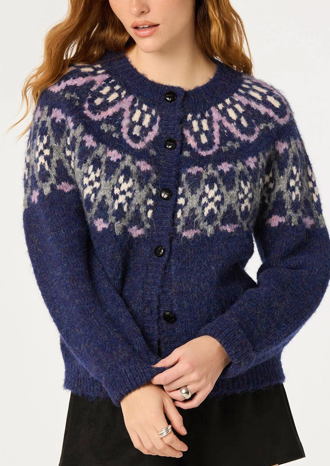 A woman wearing a navy blue knit cardigan with a Fair Isle pattern in lavender, gray, and cream, paired with a black skirt against a plain white background.