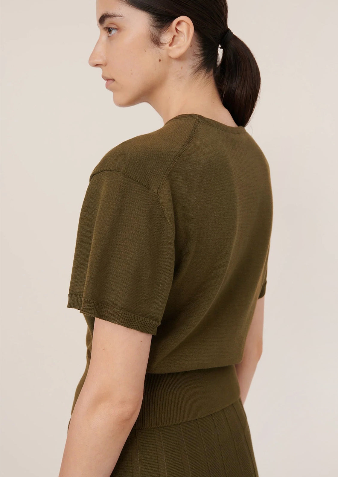 Woman wearing an olive green top against a plain background