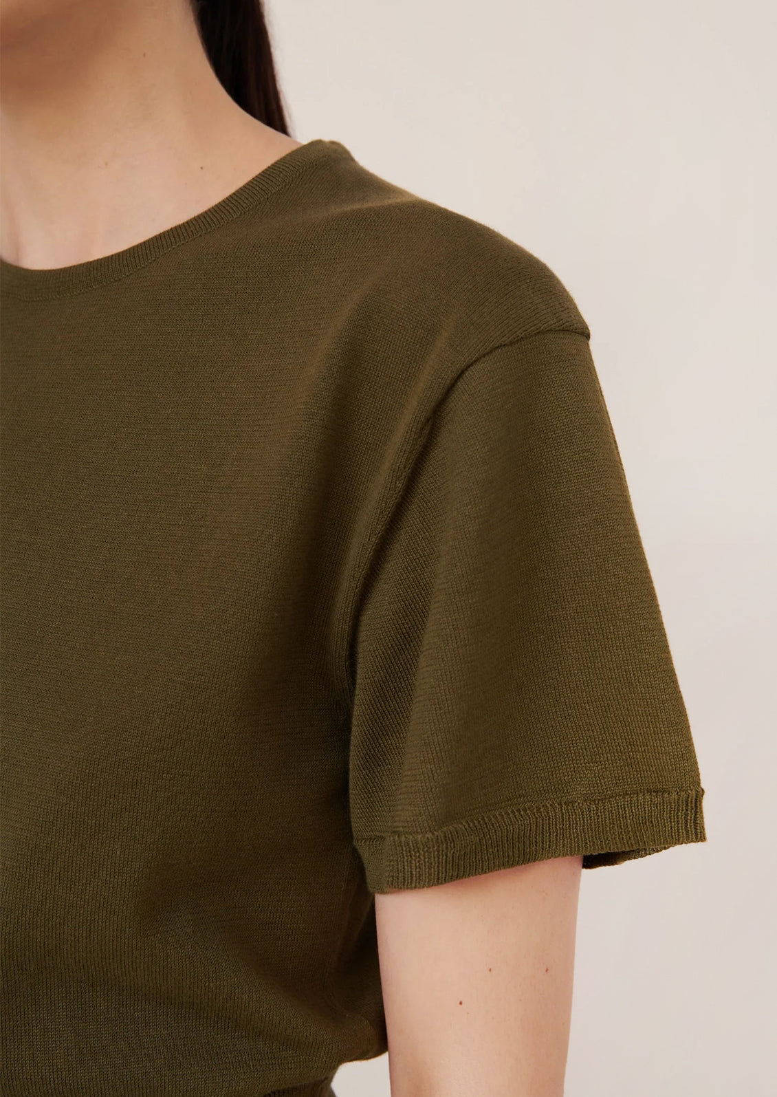 Close-up of a person wearing an olive green t-shirt against a neutral background