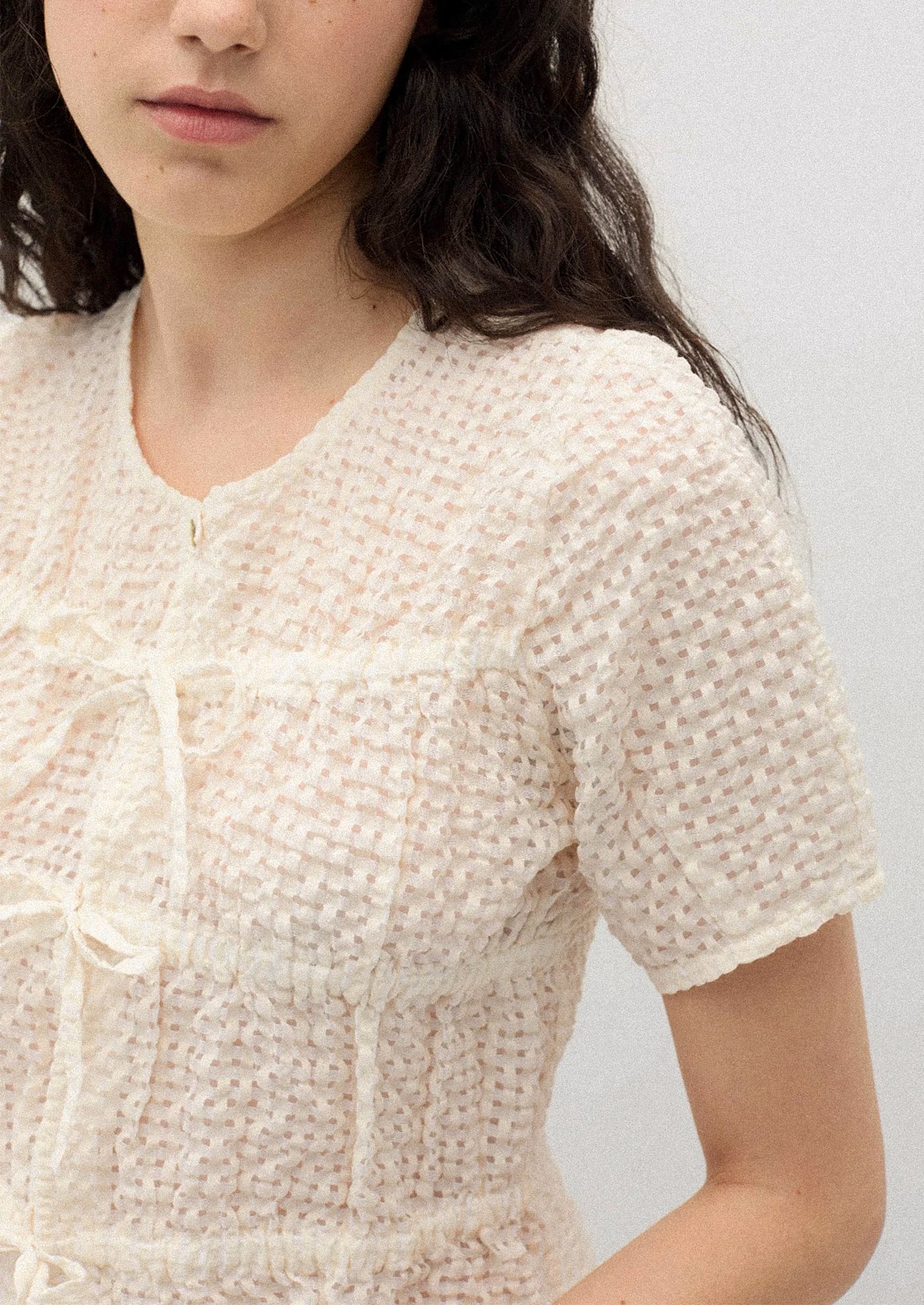 A person wearing a crinkled short sleeve top in cream.