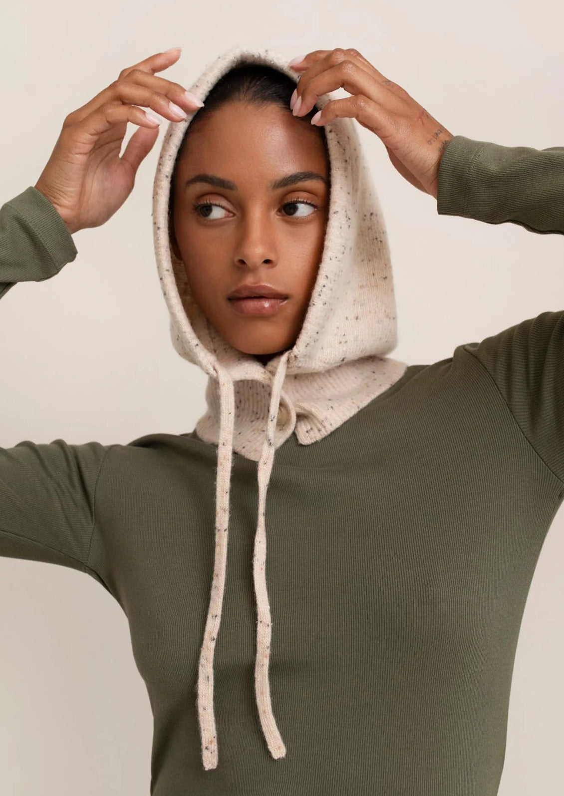 Person wearing a green hoodie with a beige hood against a plain background