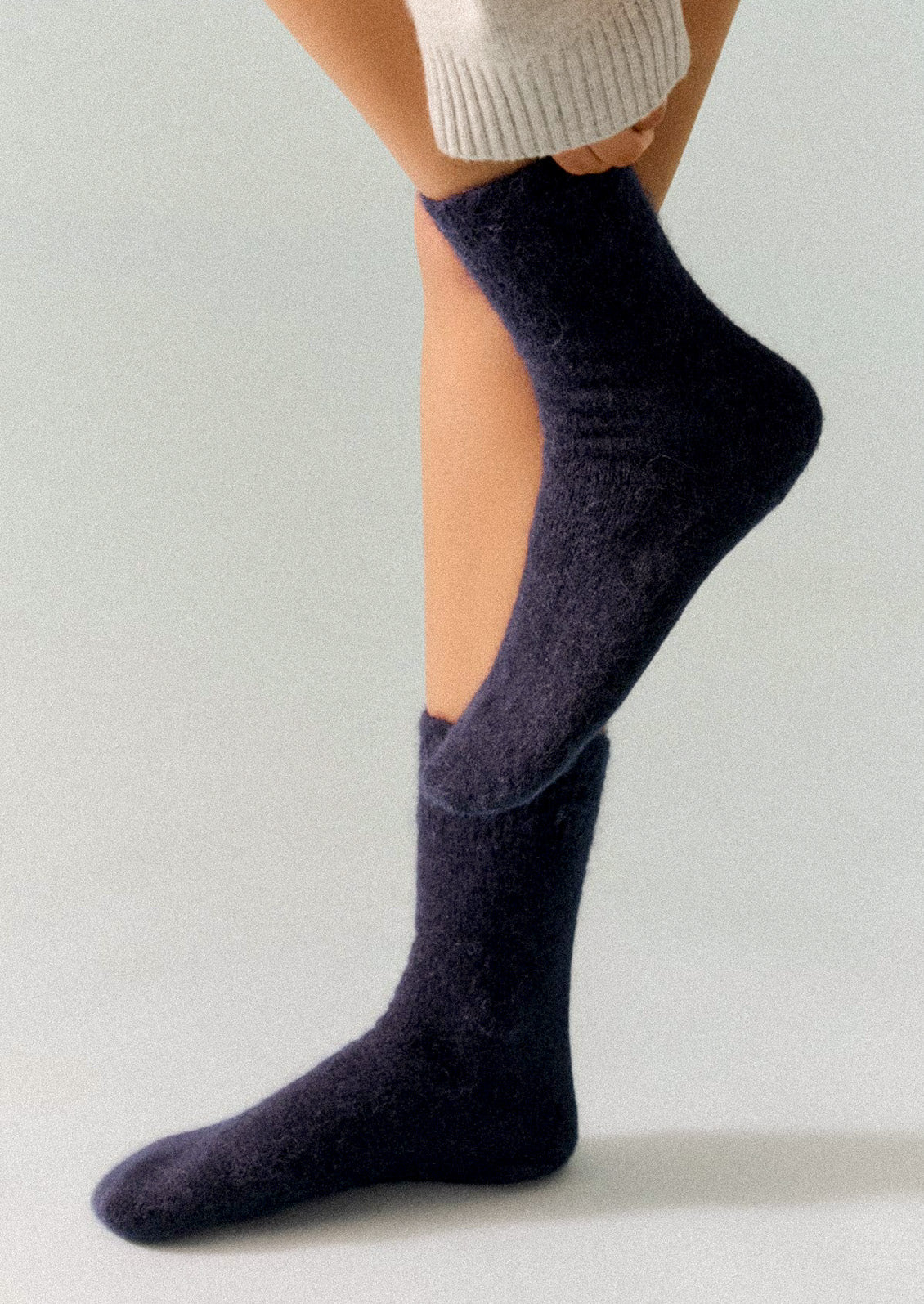 A person wearing dark navy blue alpaca blend socks with one leg lifted and pulling up the sock with their hand.