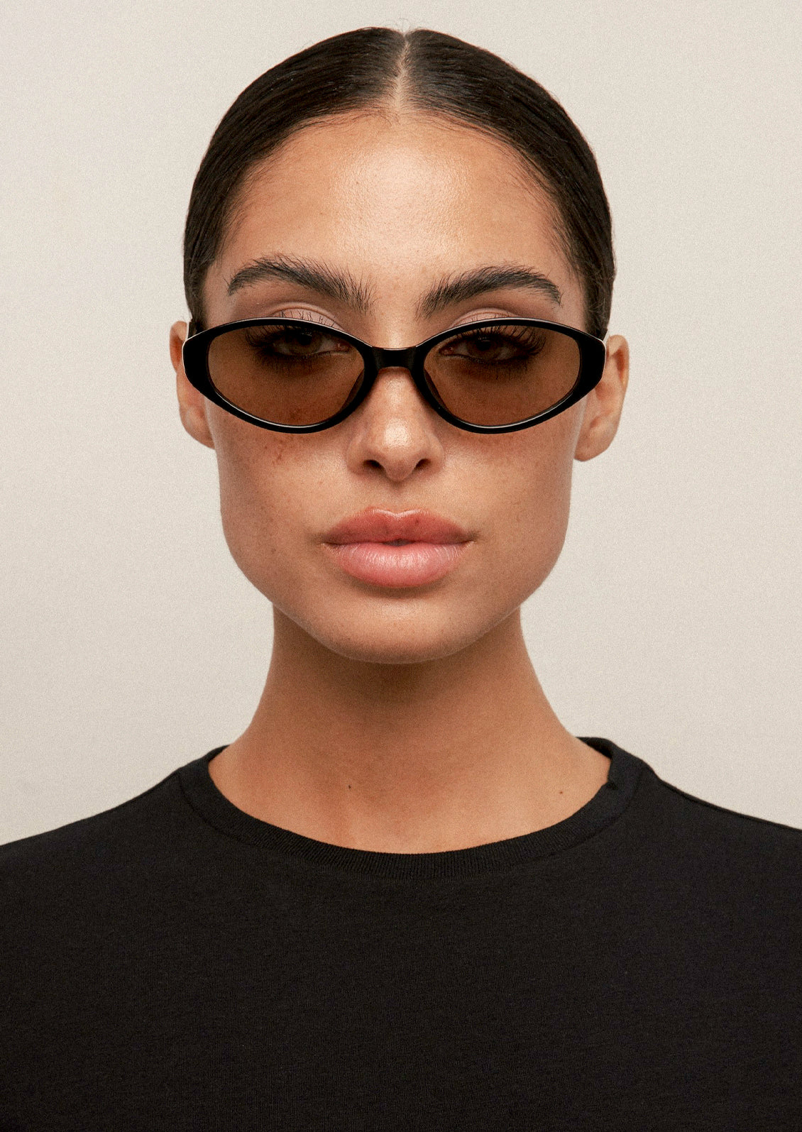 A woman wearing a pair of cat eye sunglasses with a black frame and olive lenses.