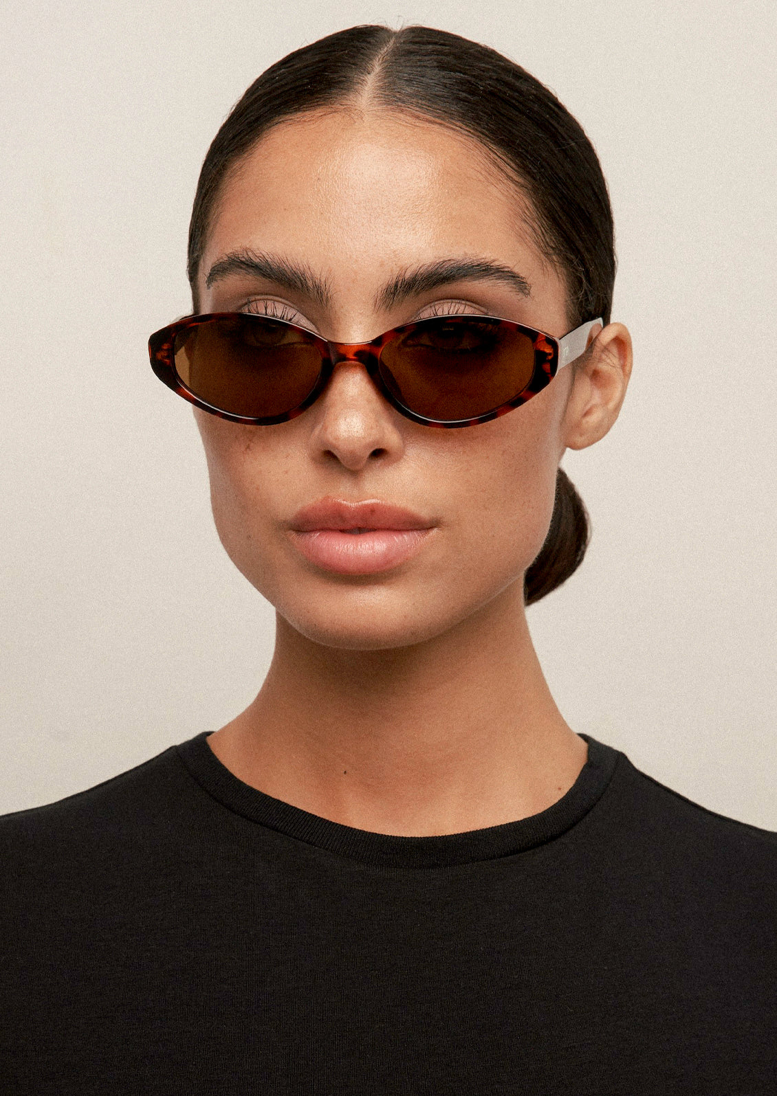 A woman wearing a pair of cat eye sunglasses with a tortoise frame and brown lenses.