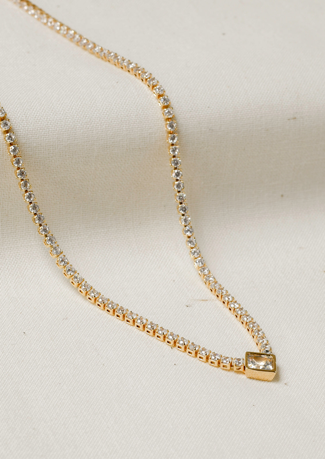 A jeweled tennis necklace with a diamond-shaped gem hanging in the center.