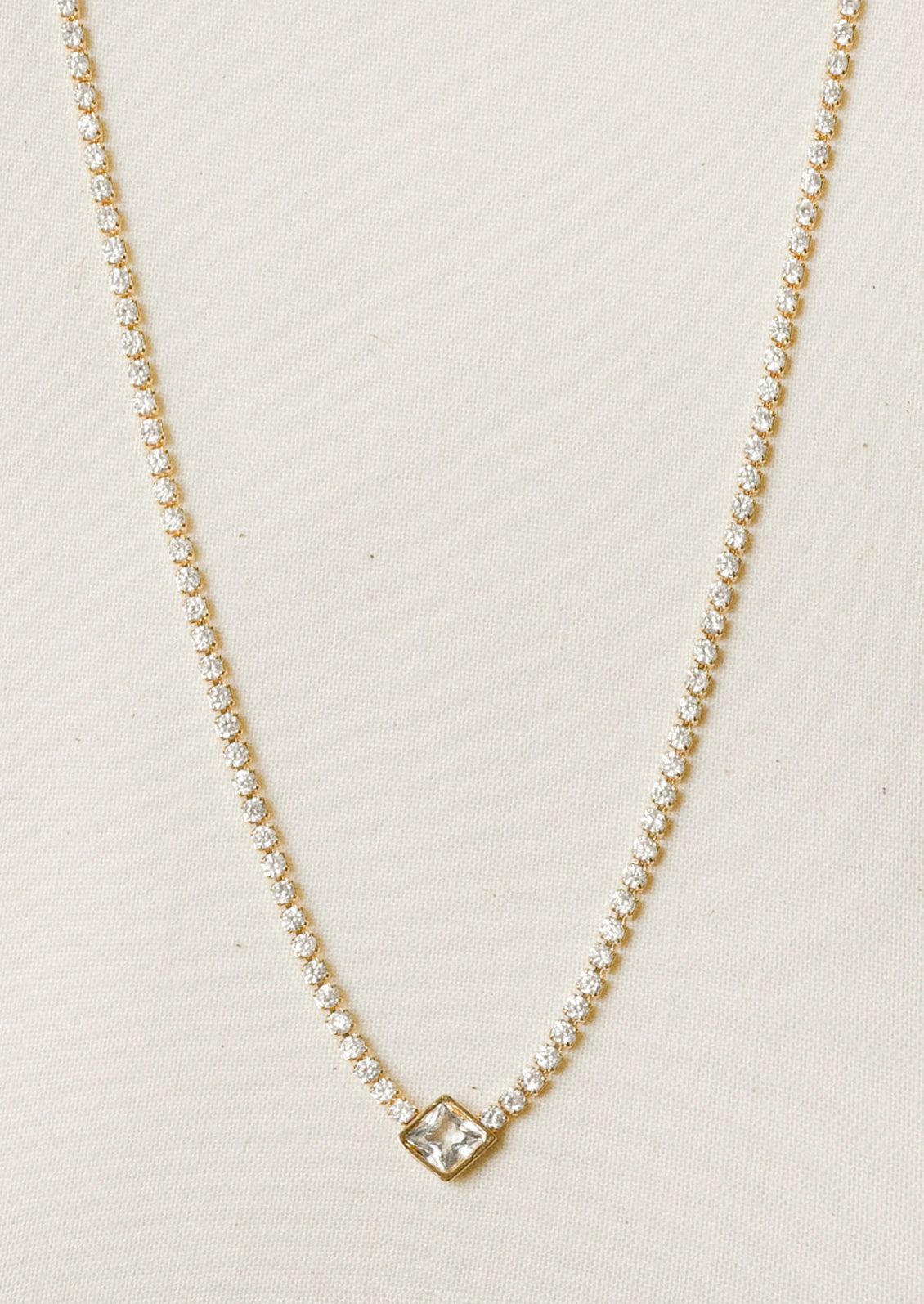 A jeweled tennis necklace with a diamond-shaped gem hanging in the center.