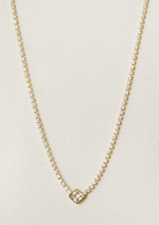 A jeweled tennis necklace with a diamond-shaped gem hanging in the center.