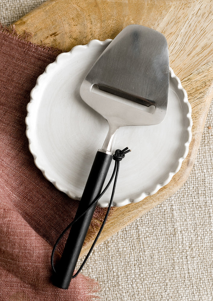 A stainless steel cheese slicer with black wood handle.