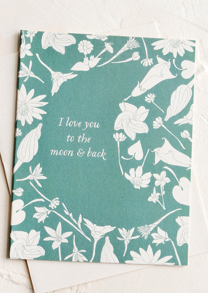 1: A greeting card with botanicals framed around moon shape, text reads "I love you to the moon & back".