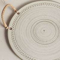 1: A round ceramic tray with neutral finish and rattan handles.