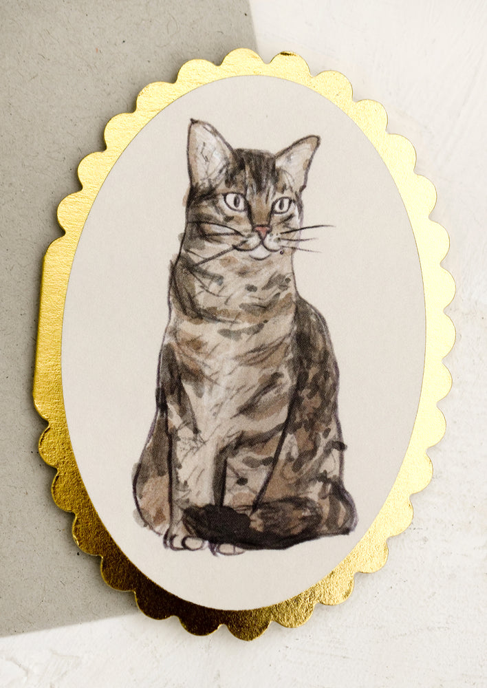An oval shaped card with scalloped gold edges and kitty illustration.