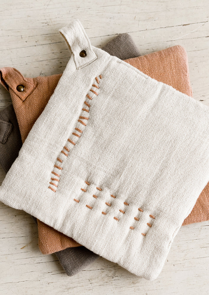 1: A stack of cotton potholders with decorative contrast stitching.