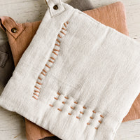 1: A stack of cotton potholders with decorative contrast stitching.