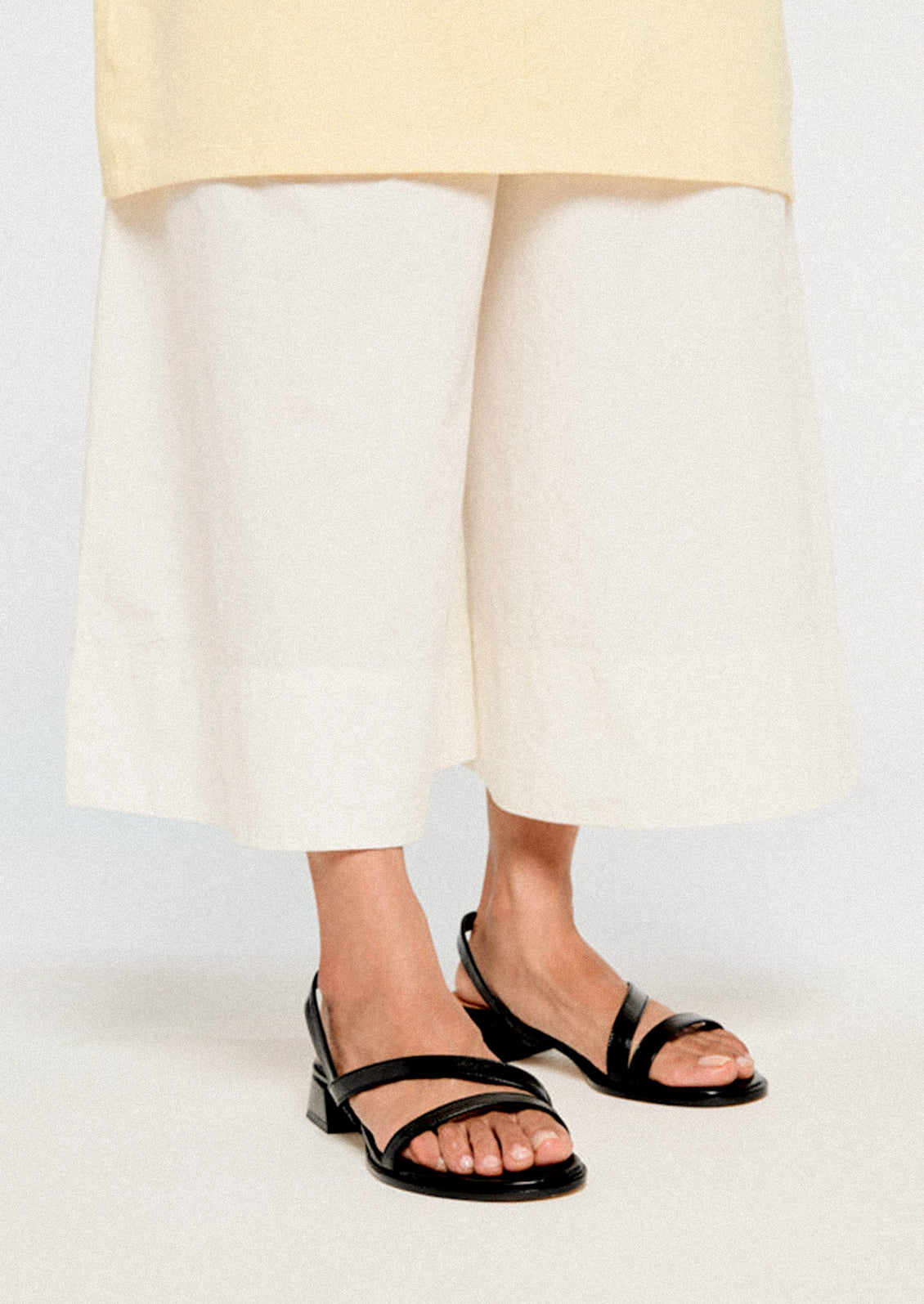 A woman wearing a pair of strappy black leather sandals with a chunky heel.