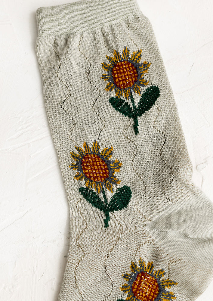 A pair of seafoam colored socks with sunflower pattern.
