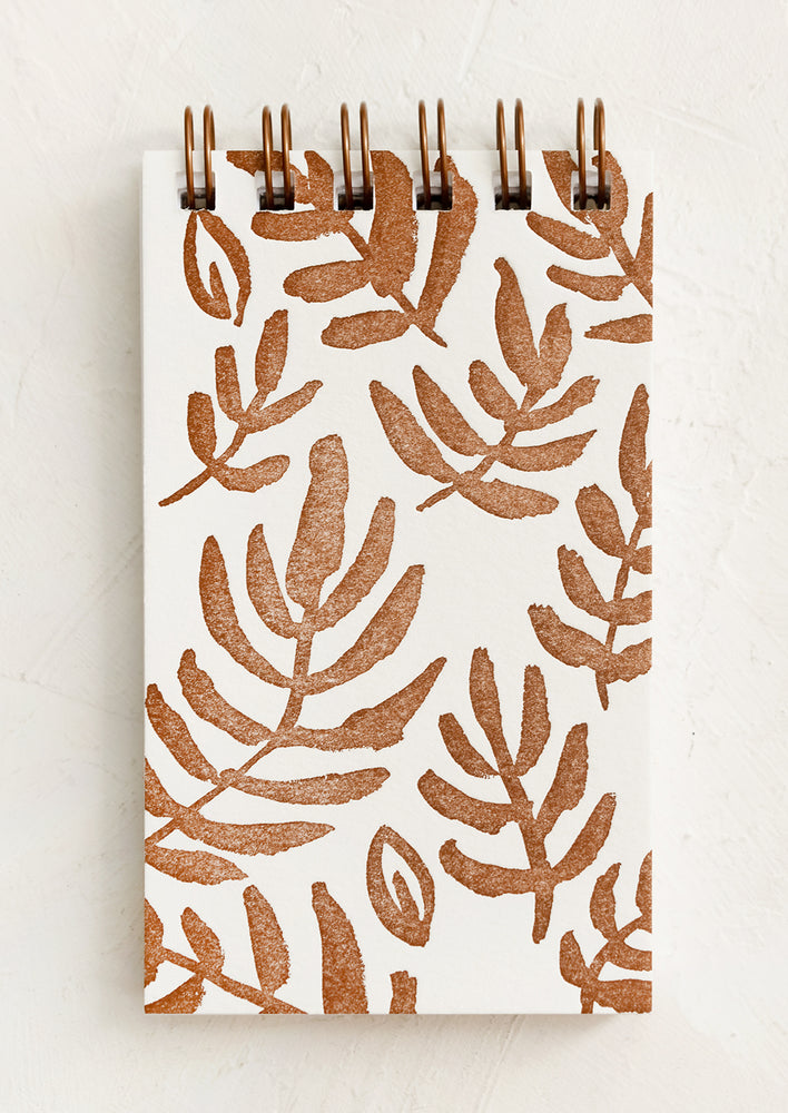 A spiral notepad with brown leaf print cover.