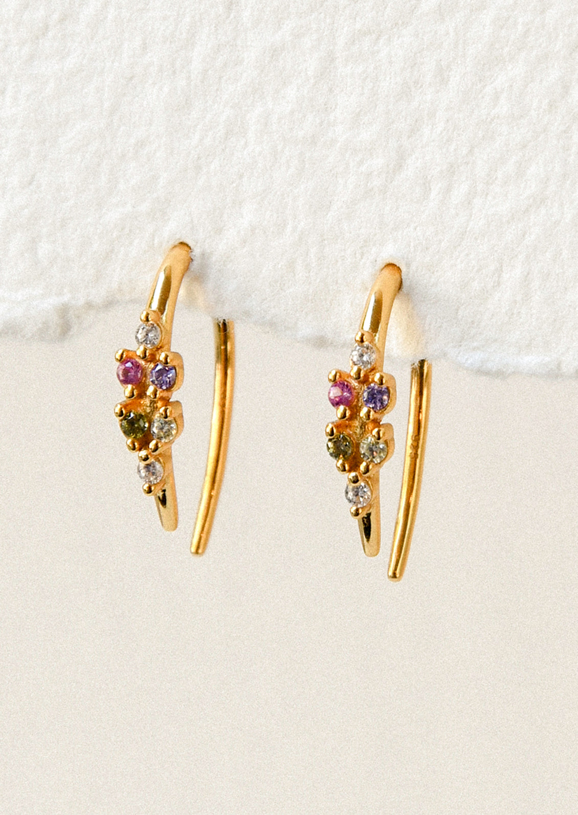 A pair of gold open hoop earrings with various colored glass stones adorned on the front.