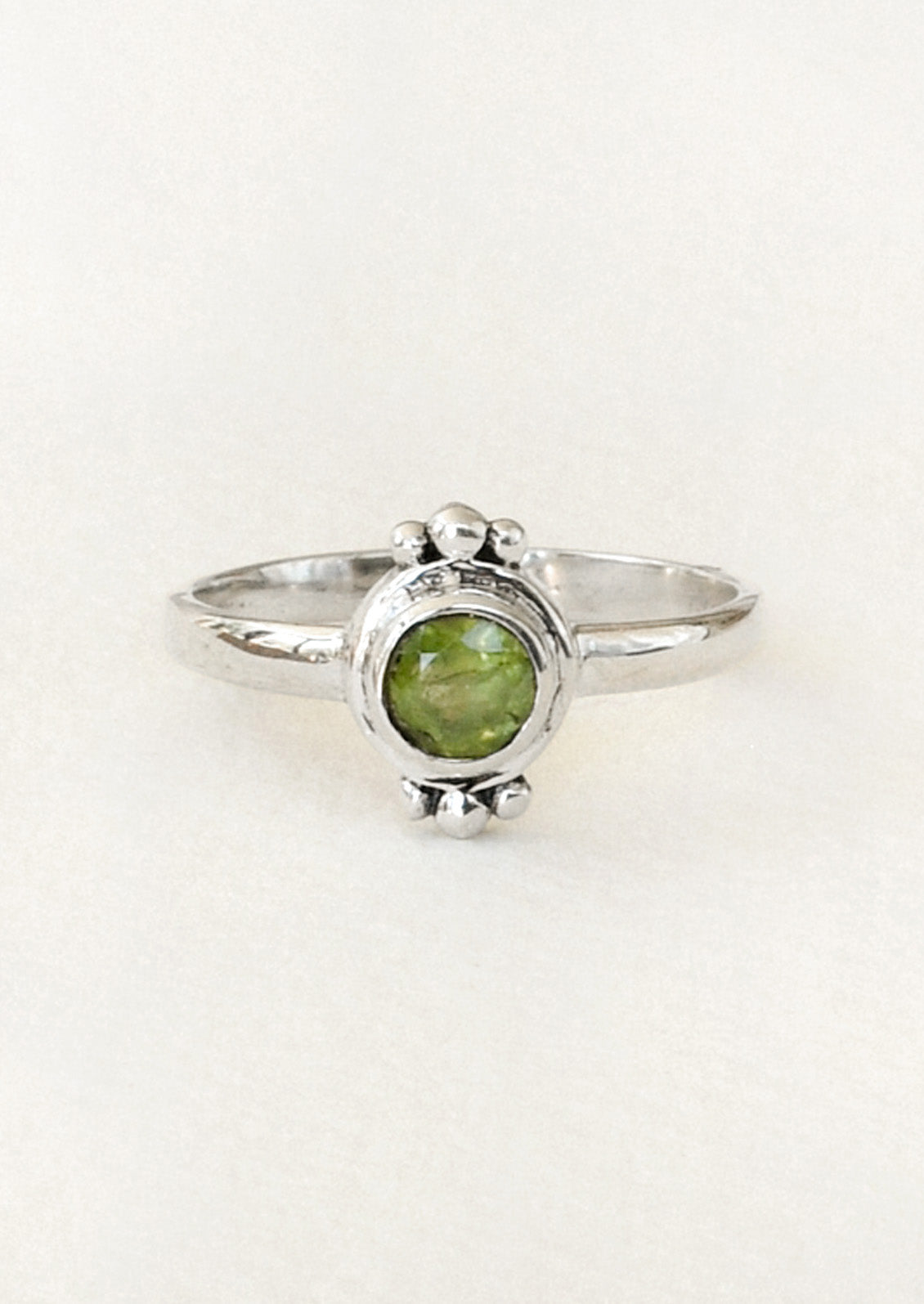 A sterling silver ring with a unique design featuring three tiny spheres on the top and bottom and a peridot gem in the center.