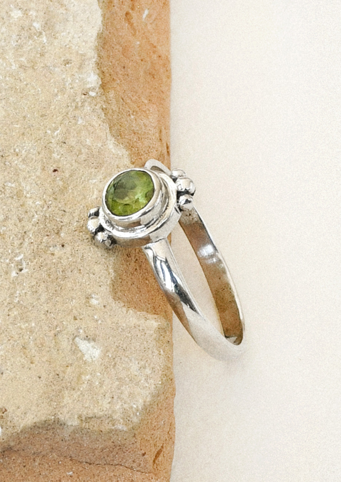 Side view of a sterling silver ring with a unique design featuring three tiny spheres on the top and bottom and a peridot gem in the center leaning in the side of a brown stone.