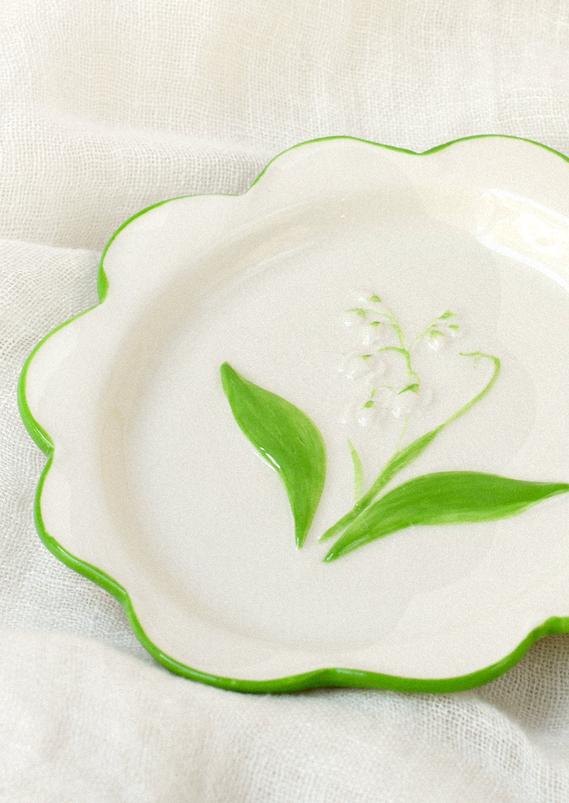 A ceramic plate with scalloped edges and a lily of the valley embossed in the center.