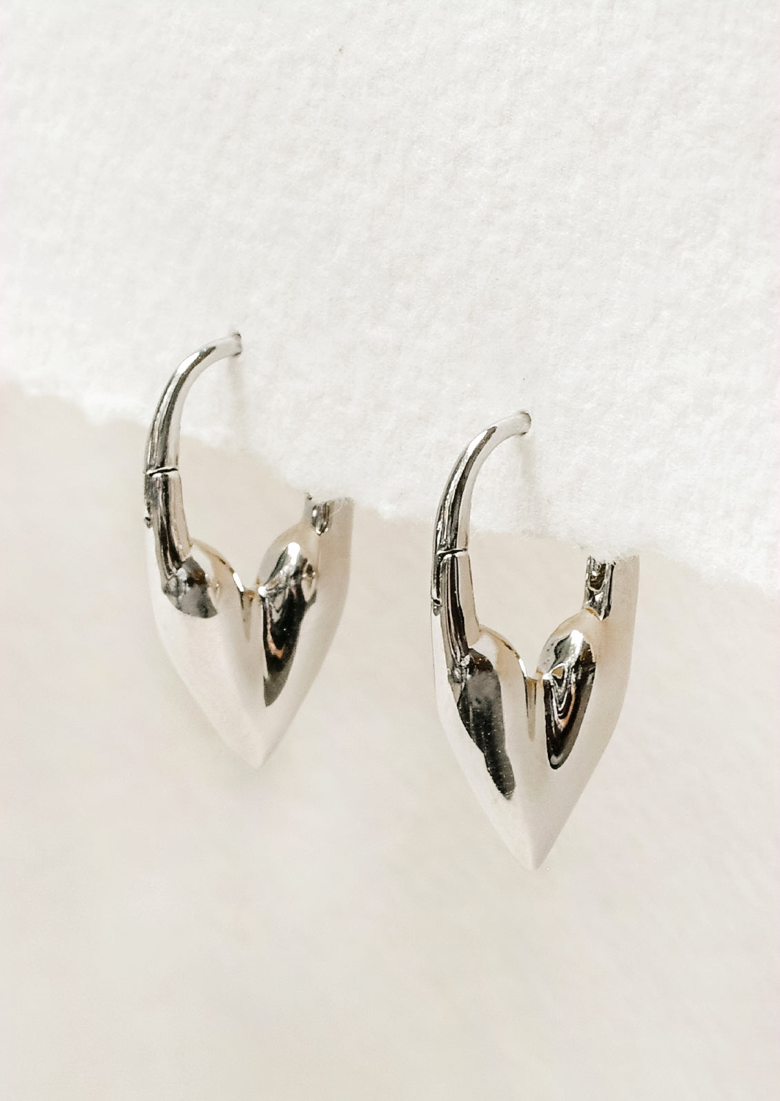 A pair of silver hoop earrings in the shape of a heart.