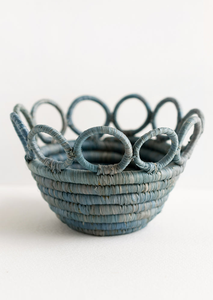 A woven raffia bowl in dusty blue color with circular cutout top rim.