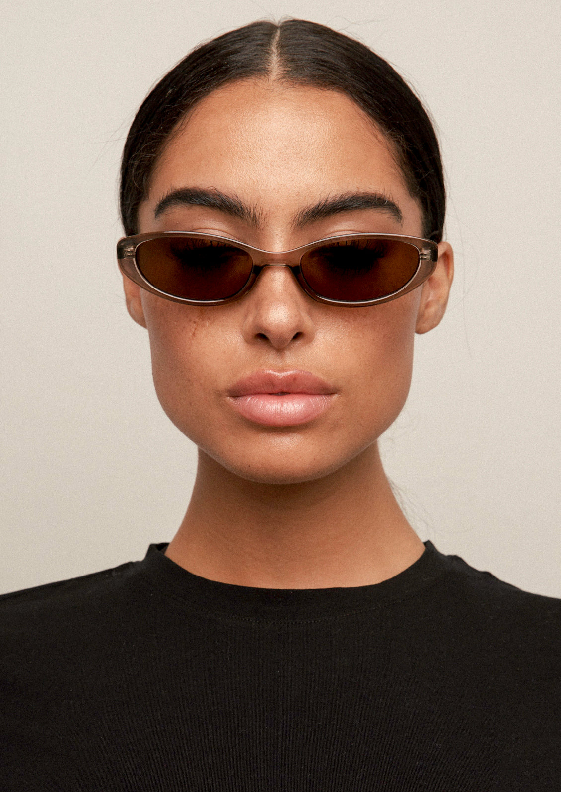 A woman wearing a pair of cat eye sunglasses with a transparent olive frame and brown lenses.